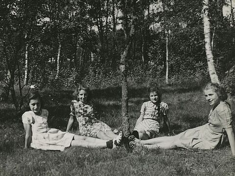 Vier Personen in Sommerkleidern mit ausgestreckten Beinen auf einer Wiese.