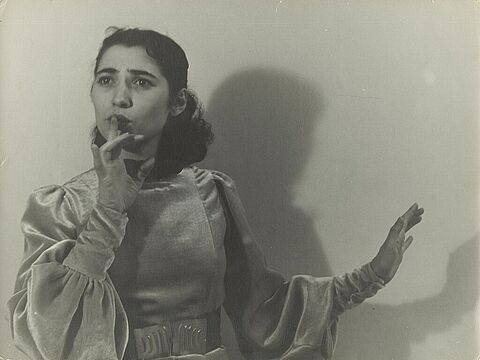 Eine junge Frau im Kostüm, die ihren Zeigefinger auf den Mund legt.