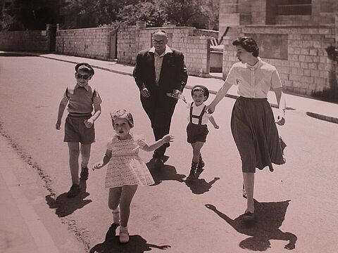 Zwei Erwachsene und drei kleine Kinder in Sommerkleidung laufen über eine Straße.
