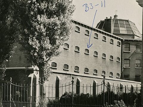 Foto eines eingezäunten, mehrstöckigen Gebäudes, darauf eine handschriftliche Markierung.