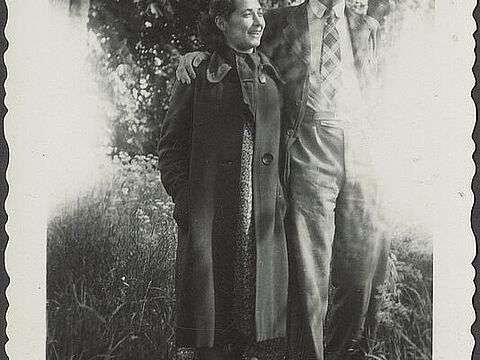 Foto mit gewelltem weißen Rand, das zwei Personen Arm in Arm vor einem Baum zeigt.