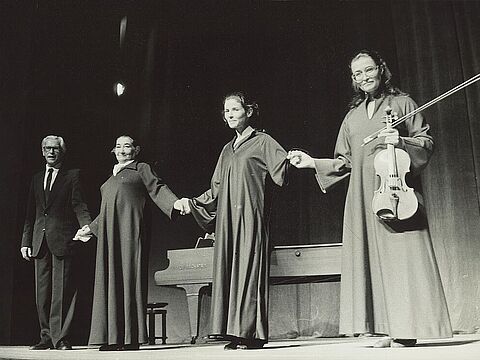 Vier Personen in langen Gewändern auf einer Bühne halten sich an den Händen.