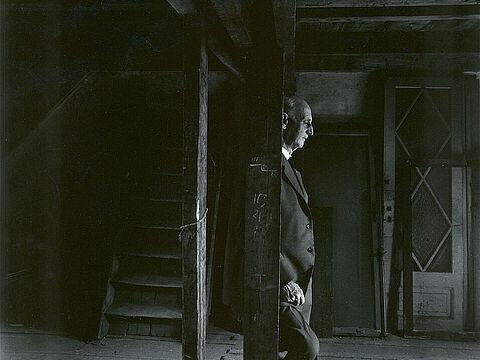 Ein Mann lehnt an einem Balken in einem leeren Zimmer und blickt zu Boden.